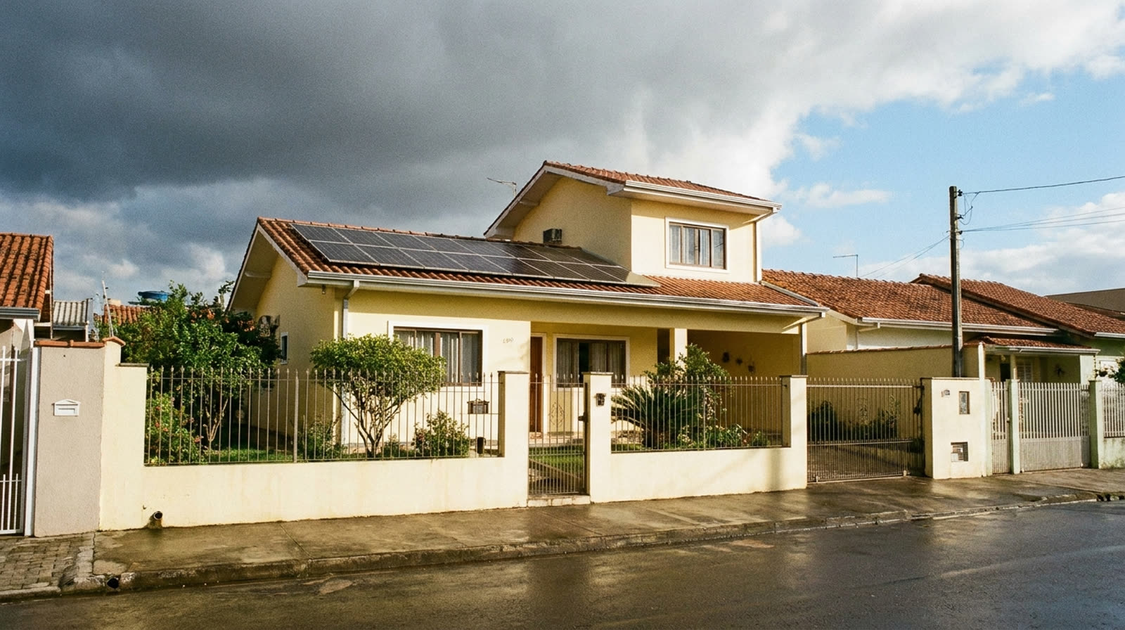 Casa de rua com placas solares sob céu dividido entre nuvens de chuva e sol