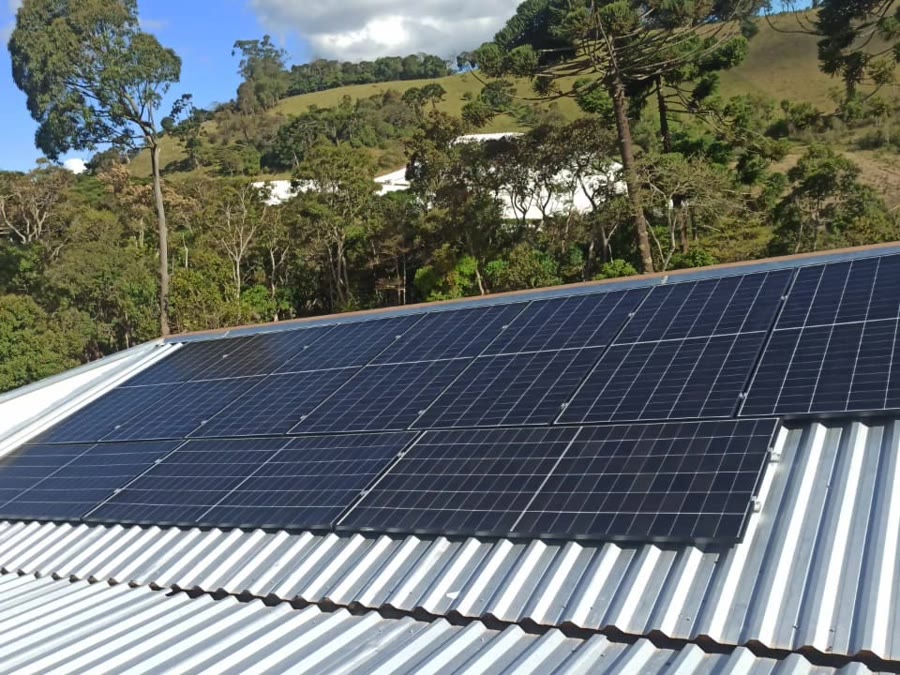 Usina solar instalada pela Sollivre no telhado metálico de um galpão em sítio de Bom Repouso, com dez módulos e a serra ao fundo